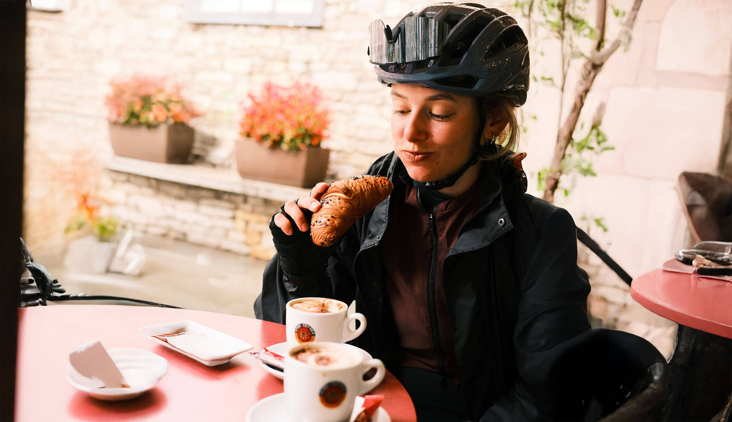 Cycliste en pause café à Annecy mangeant un croissant après une sortie vélo, moment d’encas healthy pour la nutrition sportive.