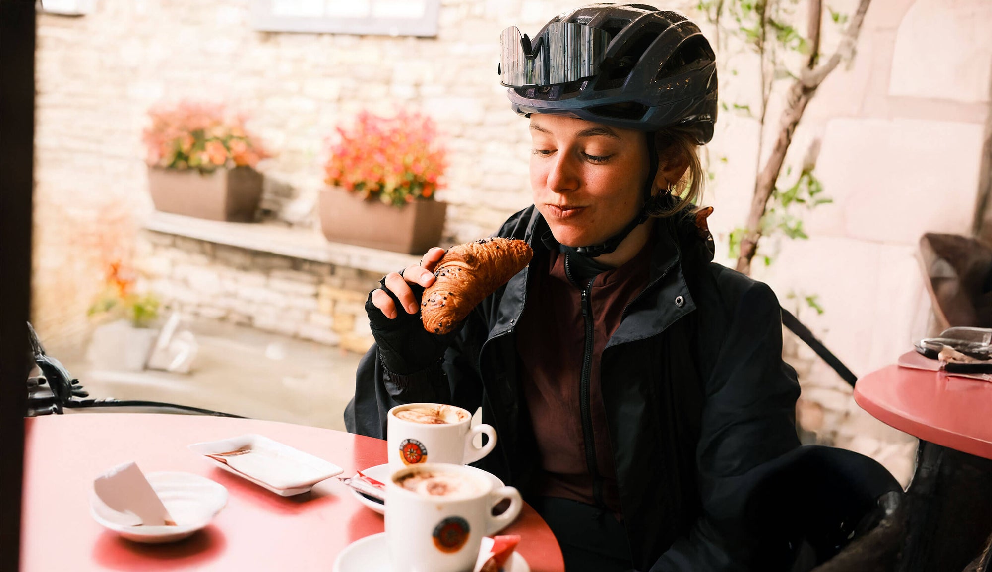 Cycliste en pause café à Annecy mangeant un croissant après une sortie vélo, moment d’encas healthy pour la nutrition sportive.
